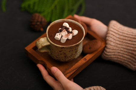 Top view, Woman hands serving a cup of tasty hot chocolate with marshmallows over black table.