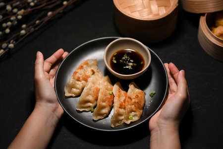 Close-up image a Female hands holding a plate of tasty fried dumplings over modern black table.の写真素材