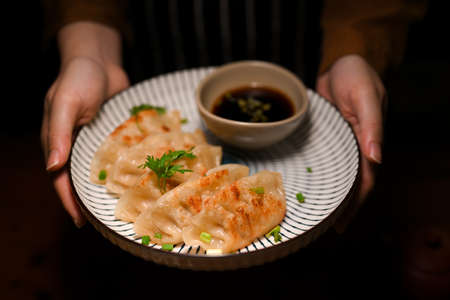 Close-up, Female hands serving a plate of tasty Asian Chinese fried dumplings with special sauce.