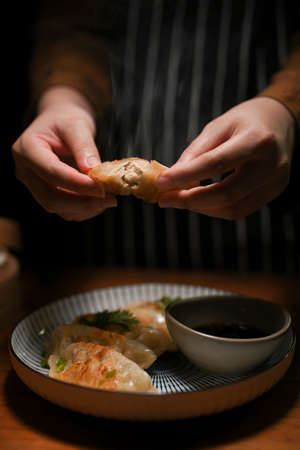 Close-up, Female hands holding a tasty Chinese fried dumpling or gyoza over a dining table. Asian gyoza conceptの写真素材