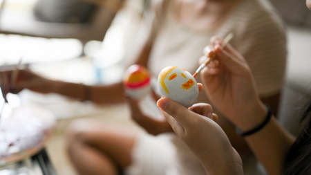 A female painting and drawing a cute face on an Easter egg. Close-up image and blurred background....