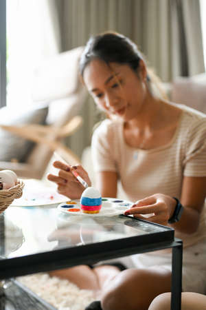 Selective focus image, Female painting an Easter egg at home. A colourful Easter egg is on a paletteの写真素材
