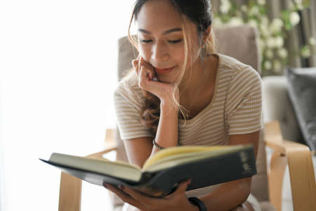 Happy beautiful woman enjoy reading a book in her comfortable home space. Inspirational activities.の写真素材