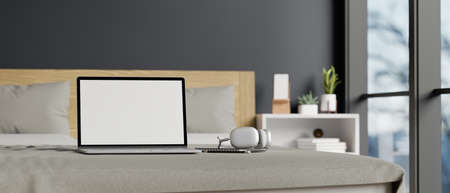 Laptop computer white screen mockup and headphone are on a comfy bed in modern and comfortable...