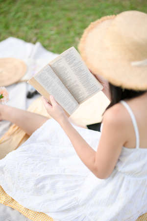 Close-up image, Charming young female in white dress, reading her favourite novel book while enjoying picnic in the green backyard.の写真素材