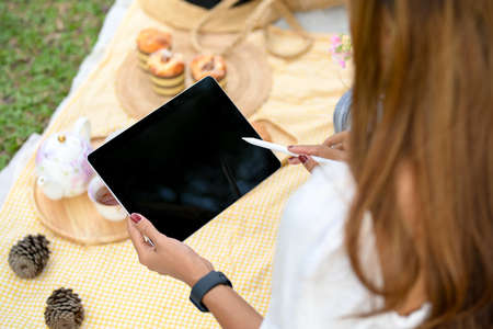 Close-up image, Female using digital portable tablet computer while having a picnic at the garden.