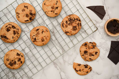 Freshly baked cookies or chocolate chip cookies on a wire cooling rack and cracked chocolate bar on...