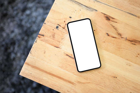 Overhead image, A smartphone white screen mockup for display your graphic image is on a wooden table