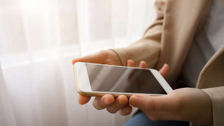 Close-up image, Female in beige suit hands holding smartphone black screen mockup in bright room.の写真素材