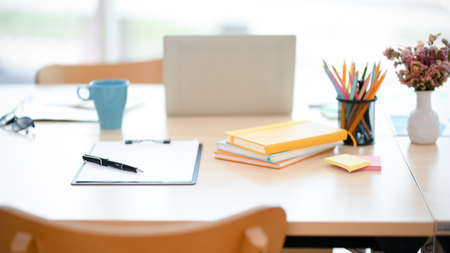 Office meeting table with clipboard and pen, stationery, coffee mug, laptop computer and decor