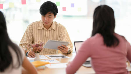 Focused Asian young male employee in the meeting with his colleagues, brainstorming and sharing...