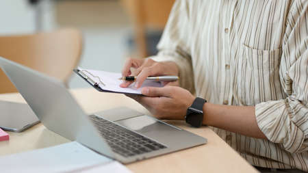 Close-up image, Male officer or businessman checking some informations on clipboard and using laptop