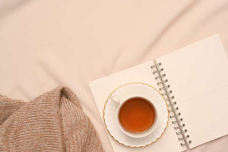 Female workspace with a cup of tea, diary book, cozy sweater and copy space on beige background.の写真素材