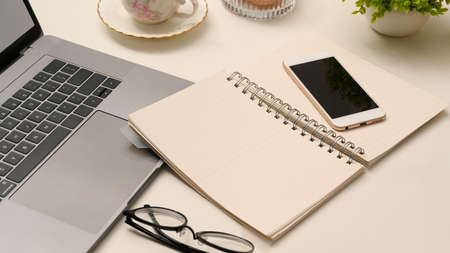 Closeup, Office desk workspace with open spiral notebook, smartphone, eyeglasses and laptop on table