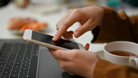 Close-up, side view, Female hands holding using smartphone at her office desk workspace.の写真素材