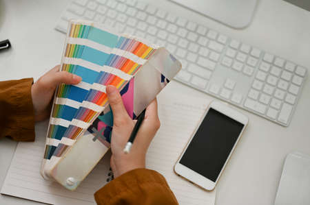 Female graphic designer selecting the colour for her graphic work on a colour palette at the desk.の写真素材
