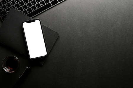 Dark office desk top view with smartphone white screen mockup, office accessories and copy space.