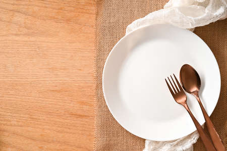 Empty white plate mockup and silverware on brown place mat and copy space on wooden background.の写真素材