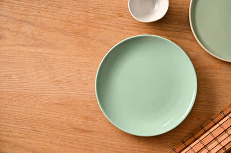 Minimal green ceramic plates mockup and space on wooden dining table background. top view, flat layの写真素材