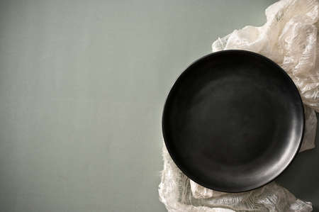 Empty black ceramic plate mockup on a white tablecloth with space on minimal grey table background.の写真素材