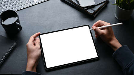 Overhead image, A man using stylus pen and working on digital tablet at his modern black workspace.