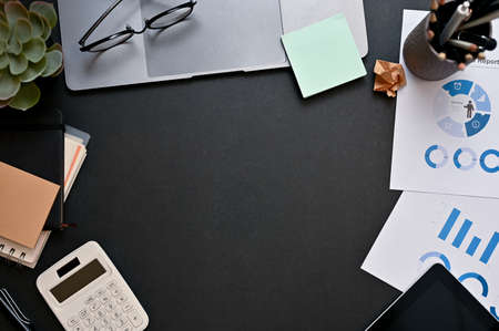 Modern black workspace background top view surrounded with office supplies, calculator, eyeglasses,...