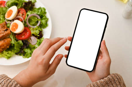 Top view, Female hands using a smartphone, searching healthy menu recipe on the internet over her...