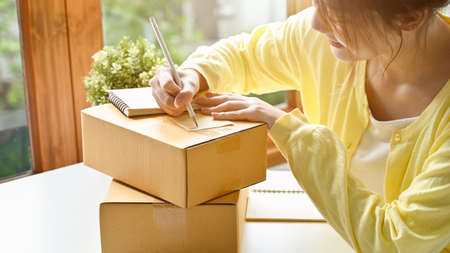 Close-up image, Beautiful asian young female writing the customer address on cardboard box, preparing the package to ship.の写真素材