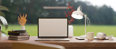 Comfortable workspace with laptop blank screen mockup, table lamp, stack of book and accessories on table over blurred green field in the background. 3d rendering, 3d illustrationの写真素材