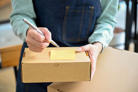 Close-up image, focus hands, Female writing a customer name and address on a small parcel box....