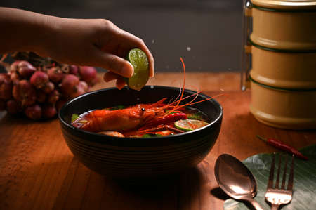 A chef squeeze a lime adding in a Thai spicy soup with shrimps, Tom Yam Kung, Thai traditional food.の写真素材