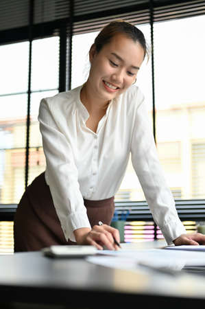 Portrait of a elegant and confident Asian businesswoman leaning on the table, reading and reviewing...