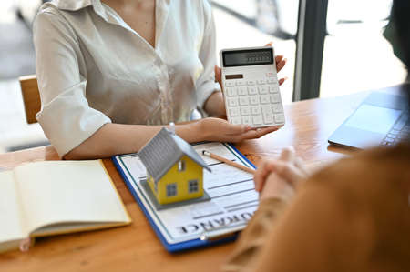 Female house insurance broker showing an insurance package price on calculator to her potential client.の写真素材