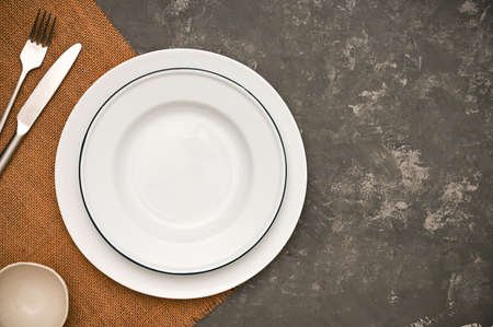Minimal white empty plate on brown placemat, silverware and copy space on stylish dark grey background. top viewの写真素材
