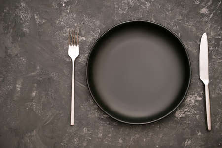 Modern stylish dining table setting with empty black ceramic plate and cutlery fork and knife on stylish dark background. top view, flat layの写真素材