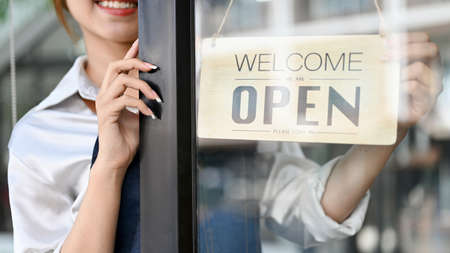 Female barista or coffee shop owner hanging an open welcome sign on the entrance door. Coffee shop,...