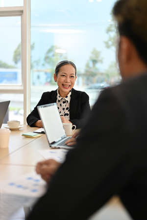 Positive Asian aged female boss or executive manager talking with male financial analysts manager in the meeting.の写真素材