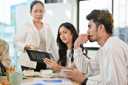 A group of graphic designers and web developers are in the meeting with aged senior female executive...