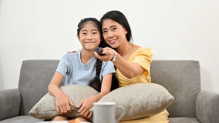 Asian young mom watching TV with her lovely daughter in the comfortable living room. Family activity...