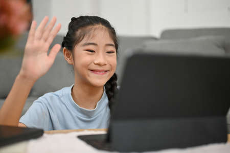 Happy Asian young little girl saying hi greeting her friends and teacher, enjoy studying on online...