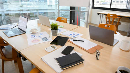 Messy office meeting table with notebook laptop, tablet, paperwork, stationery, calculator and stuff