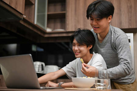 An attractive young Asian gay man tries to feed a snack to his boyfriend while his boyfriend is...