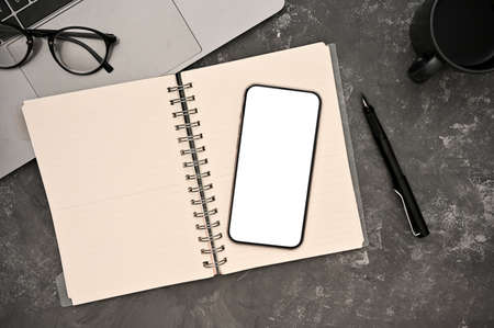 Workspace top view with smartphone white screen mockup, spiral notebook, pen, glasses, laptop and...