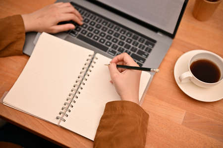 Top view, Female university student doing her homework, writing and lecturing on school notebook while studying online on laptop computer.の写真素材
