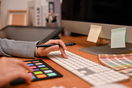 A successful female graphic designer holding a stylus one, typing on computer keyboard, and using a colour checker board. cropped imageの写真素材