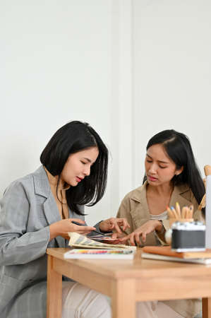 Portrait, Two professional asian female graphic designers examining a colour swatches palette, discussing the designing detail of their project together.の写真素材