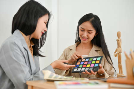Professional Asian young female graphic designer working with her coworker, examining the colour on colour checker chart together.の写真素材