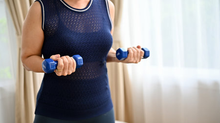 Cropped image, Active asian aged woman doing an easy body weight training at home, lifting a small...