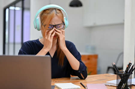 Sad teen woman wearing a wireless headphones, listening to music from smart phone while sitting in...