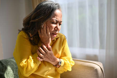 Asian aged woman touches cheek suffering from sudden tooth pain. Old lady with tooth painful...